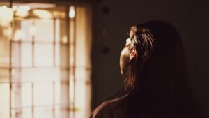 Jezelf kwijt zijn symptomen: vrouw staart peinzend uit het raam in avondlicht
